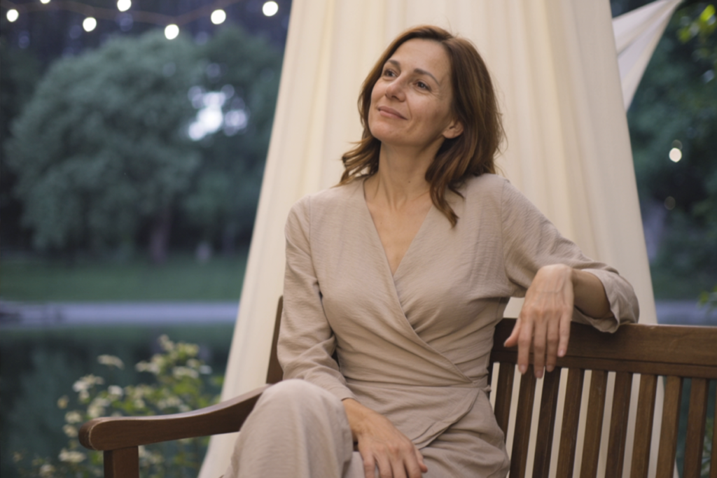 Woman sitting under soft evening lights, gazing upward in quiet reflection, embodying emotional awakening and reclaimed desire in a romantic story for women.